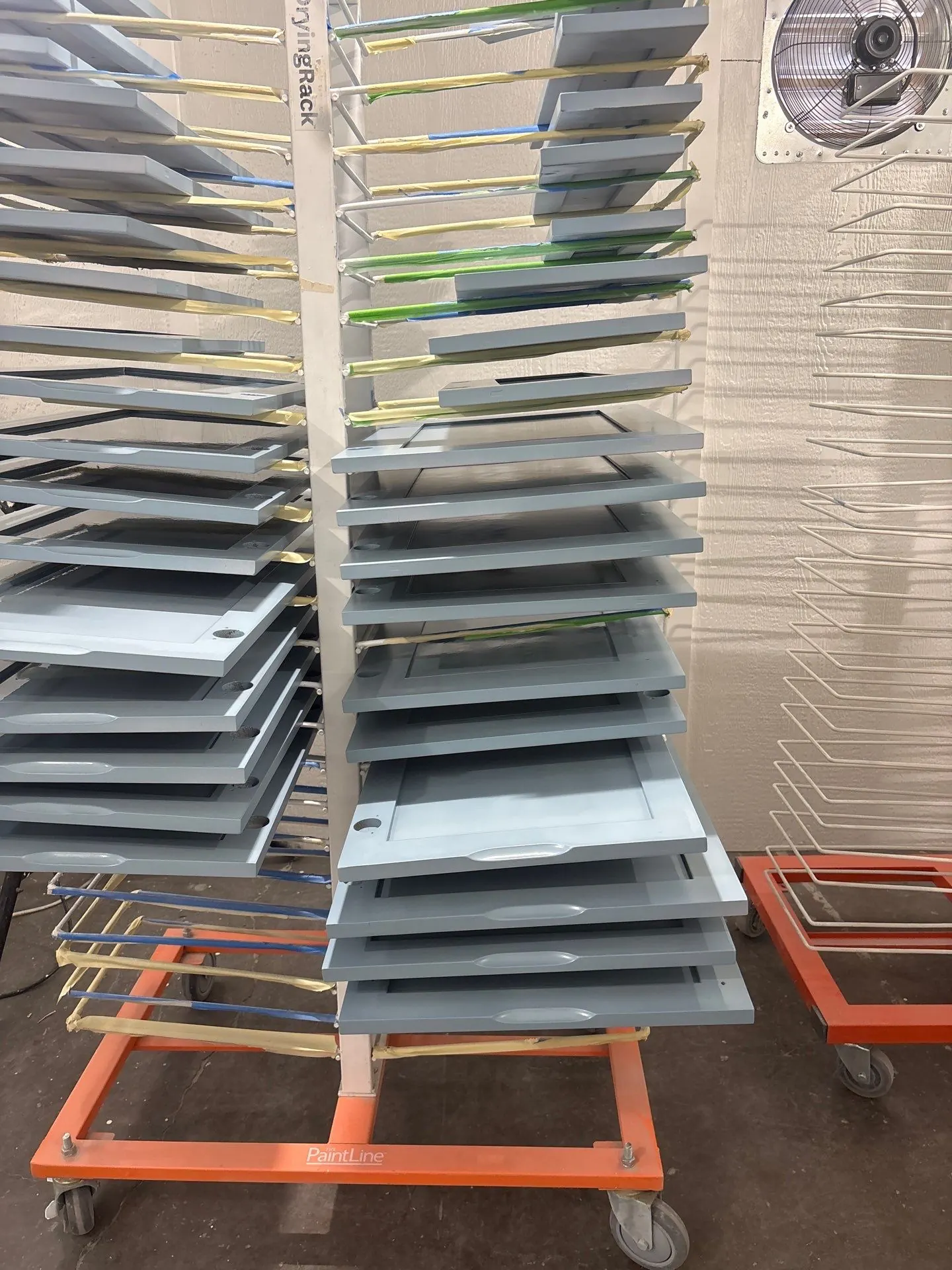 Cabinet doors and drawers stacked on rolling drying racks to cure in the Kind Home paint shop